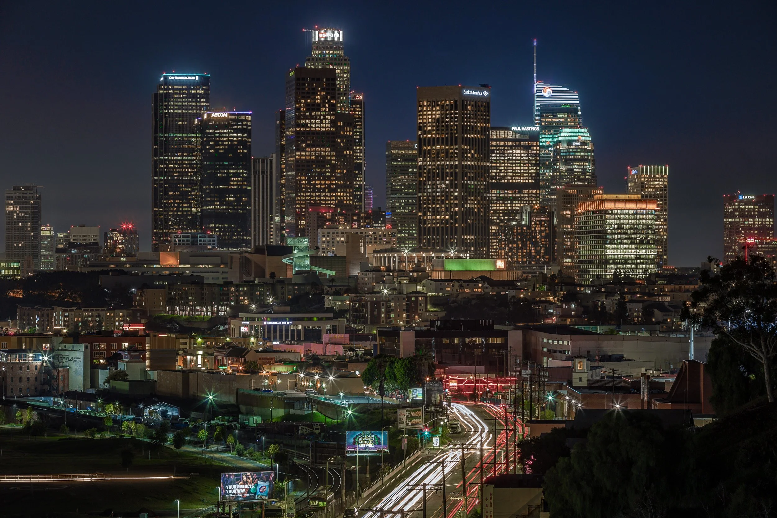 Illuminated Downtown Los Angeles skyline skyscrapers and street traffic light trails at night by Chris Ewen Crosby.