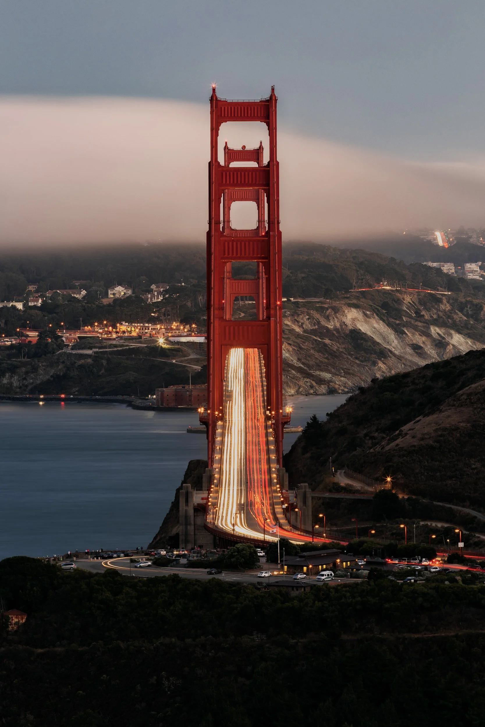 Symmetrical long exposure looking down the roadway of the Golden Gate Bridge with glowing traffic light trails and fog by Chris Ewen Crosby.