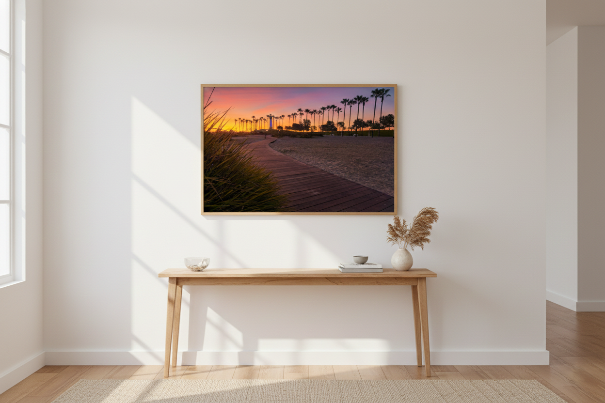 Horizontal framed Long Beach lighthouse sunset print hanging above a minimalist wooden console table with pampas grass decor.