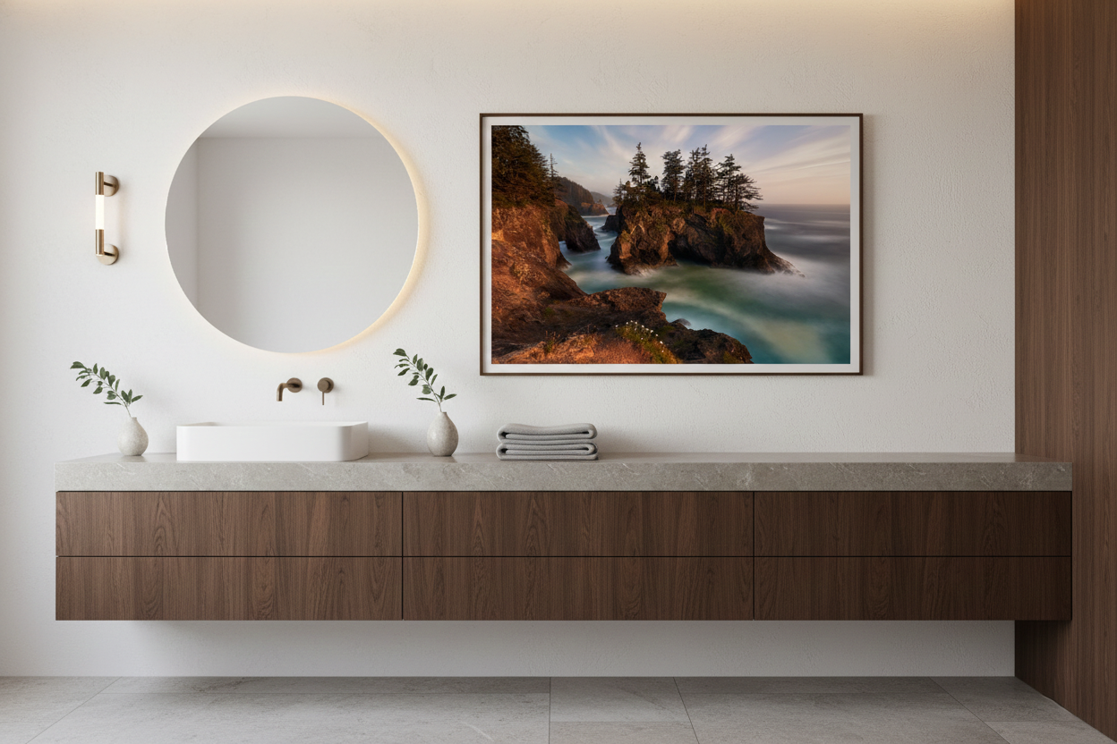 Framed Natural Bridges Oregon Coast framed photography print hanging above a floating dark wood bathroom vanity and illuminated round mirror.