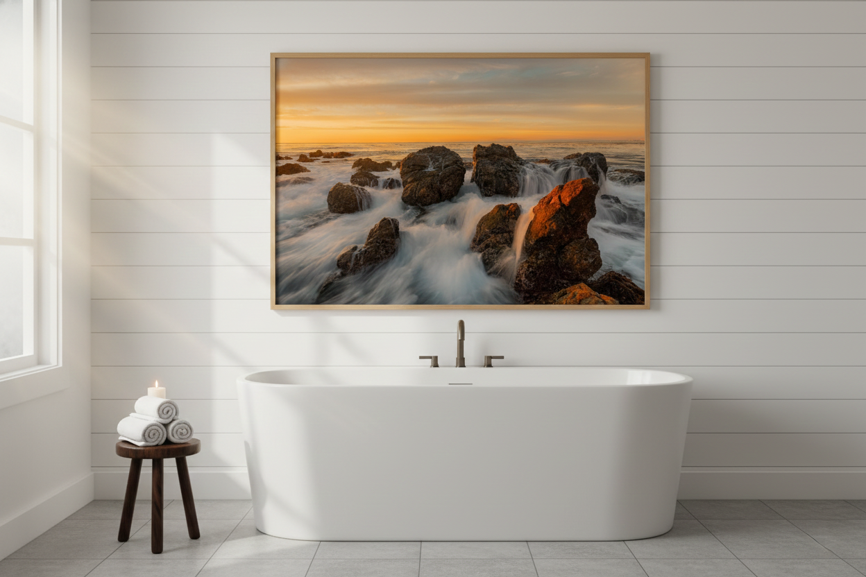 Large framed California rocky coast sunset photo print hanging above a modern freestanding bathtub on a white shiplap wall.