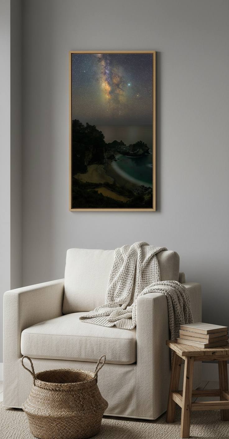 Light wood framed McWay Falls night landscape print hanging in a cozy reading corner beside an armchair with a woven basket.