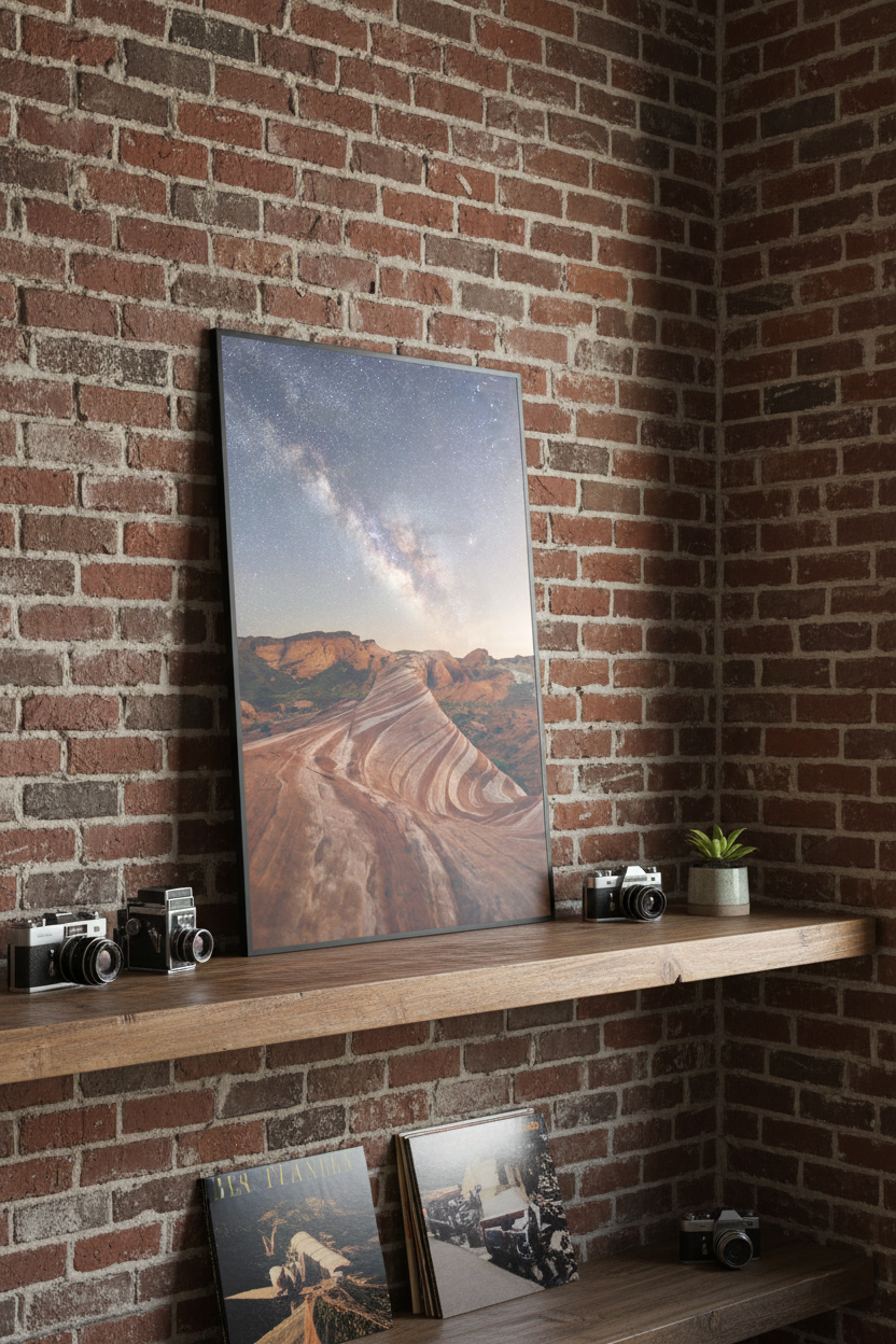 Framed Valley of Fire night landscape art print resting on a wooden floating shelf against a red brick wall with vintage cameras.
