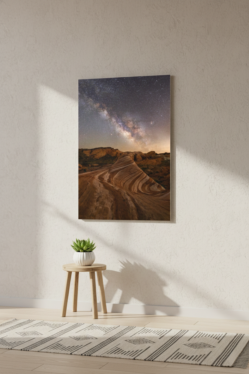 Unframed canvas print of Valley of Fire under the Milky Way hanging on a textured off-white wall over a small wooden stool.