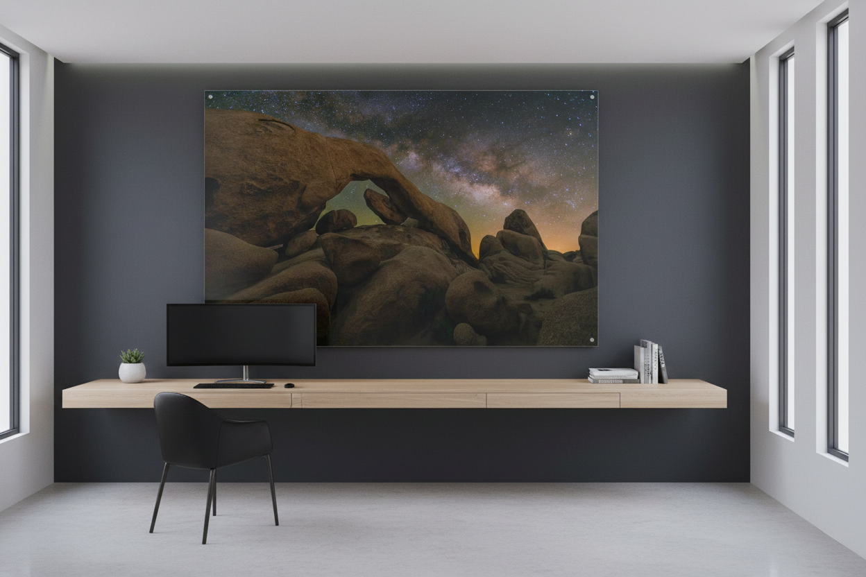 Large horizontal acrylic print of Joshua Tree Arch Rock Milky Way mounted on a dark charcoal wall above a floating wood desk.