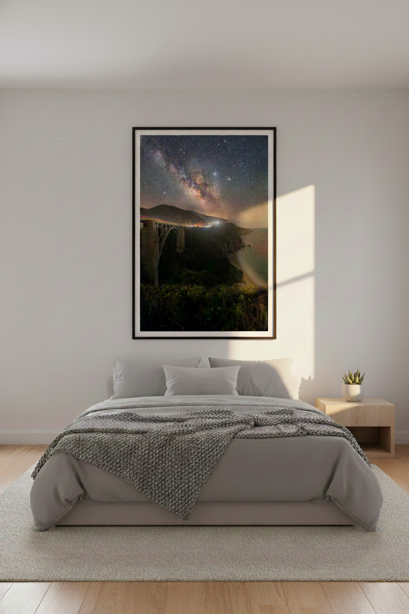 Framed vertical night landscape photograph of Bixby Bridge under the stars mounted over a modern upholstered bed.