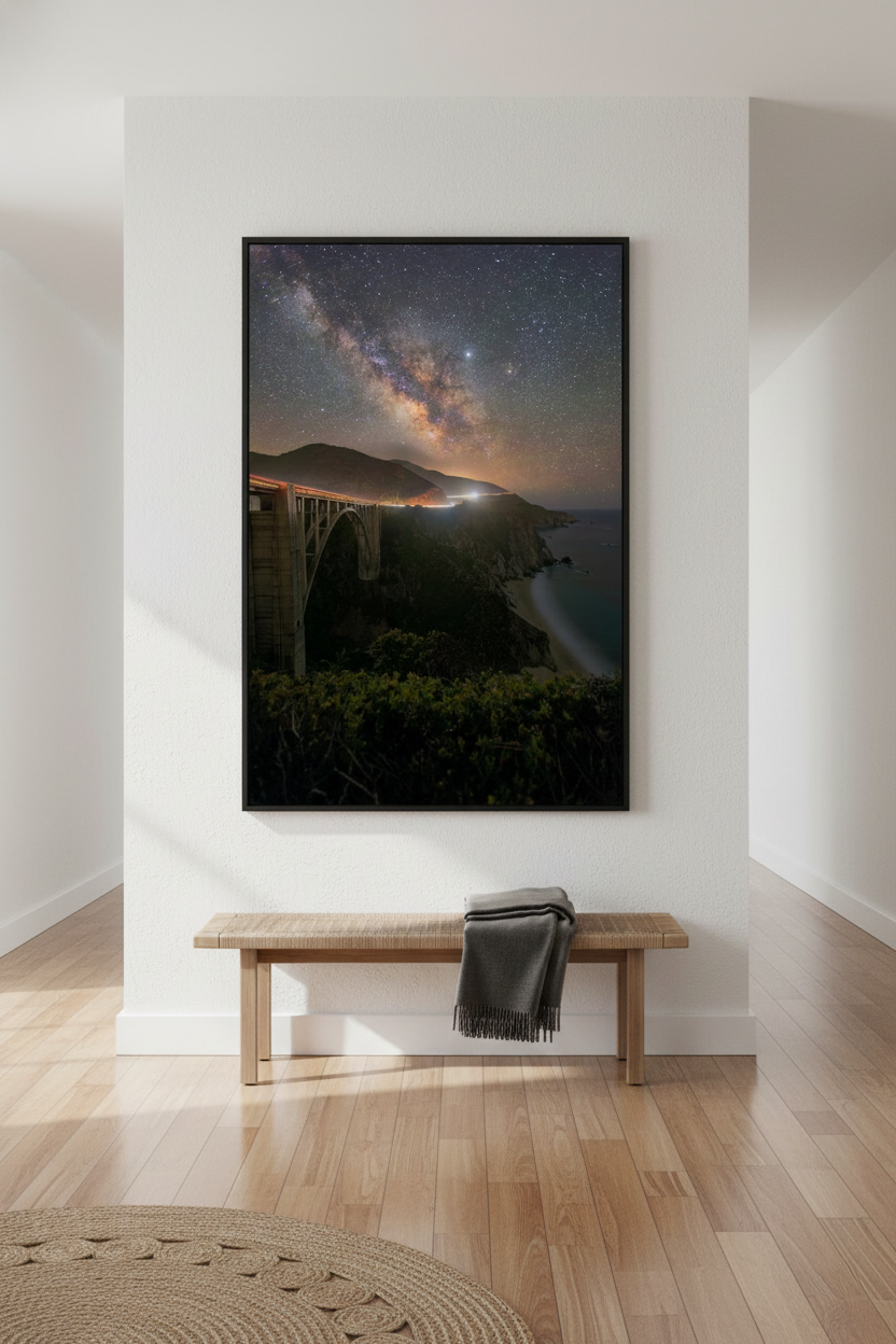 Vertical framed fine art print of Big Sur coastline at night featured on a white gallery accent wall above a minimalist wooden bench.