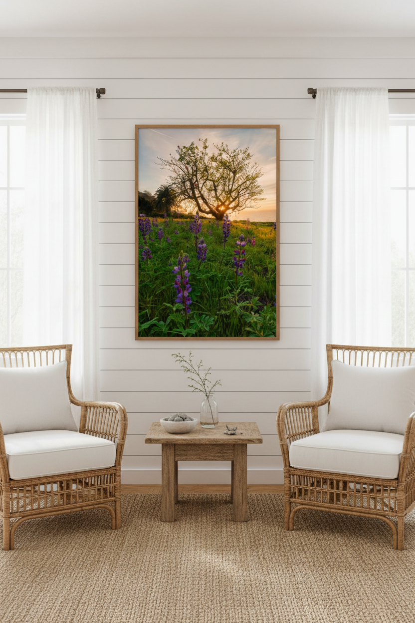 Framed coastal wildflower landscape photograph centered on a white shiplap wall between two woven rattan armchairs.