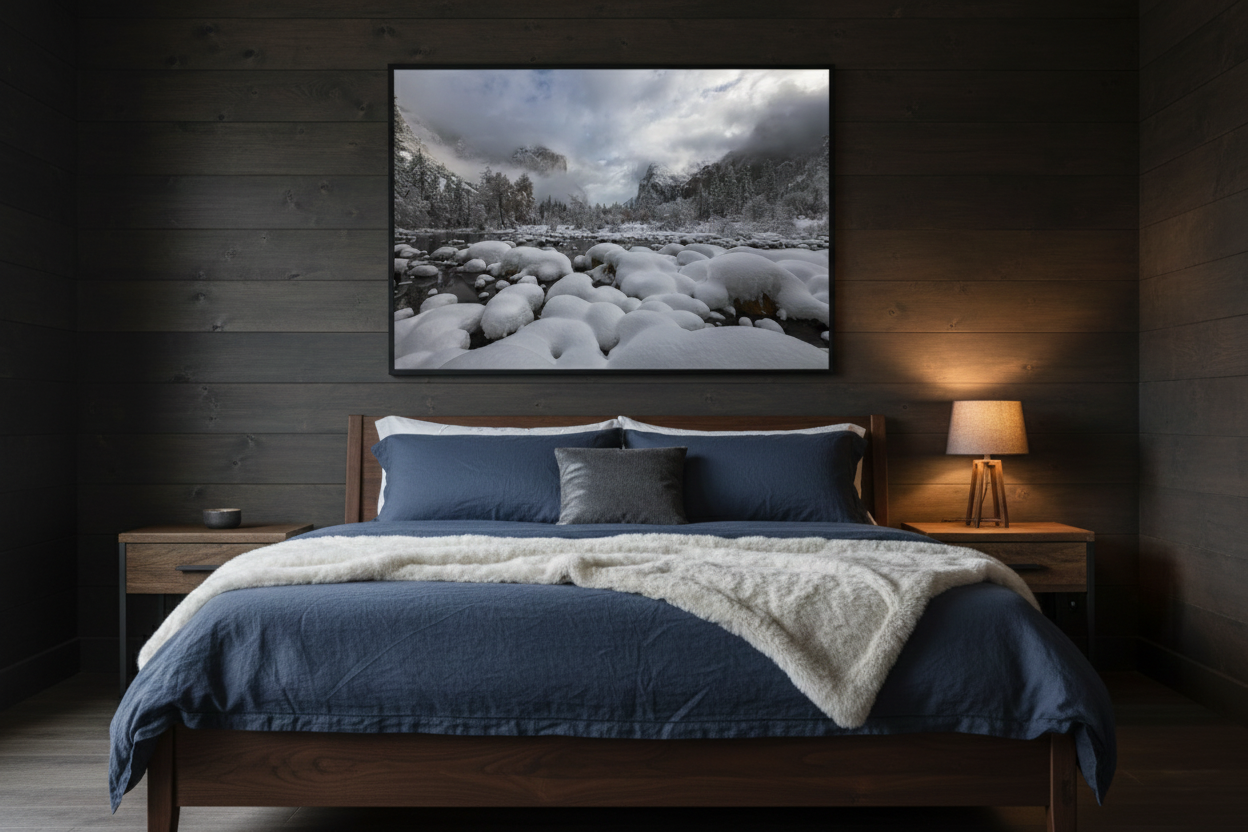 Fine art photograph of snow-covered Yosemite rocks mounted above a walnut bed frame with blue bedding against a dark wood wall.