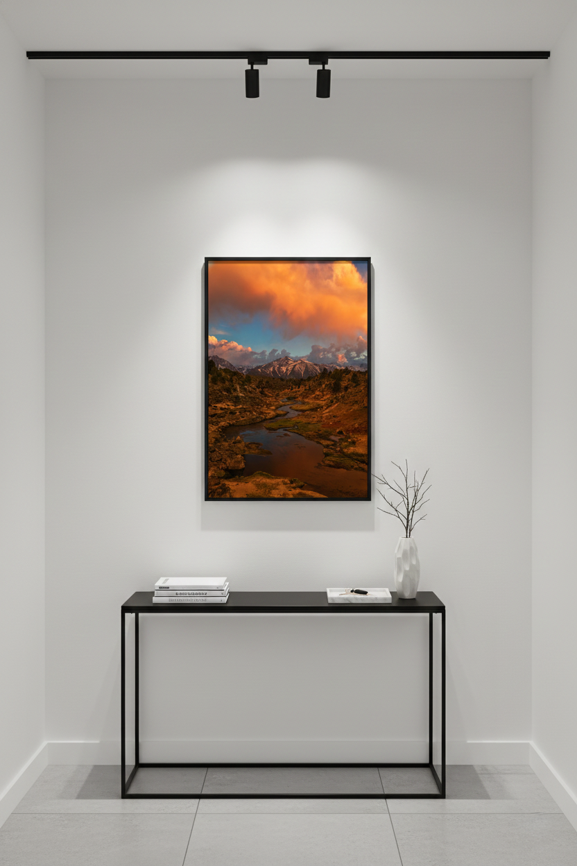 Framed Hot Creek landscape fine art print lit by overhead track lights above a black metal console table in a modern hallway.