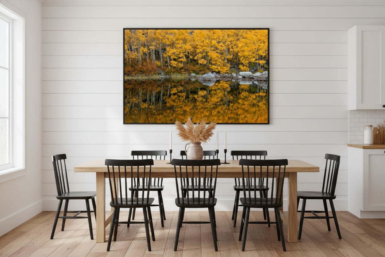 Panoramic autumn landscape print centered on a white shiplap dining room wall above a wooden table with black spindle chairs.