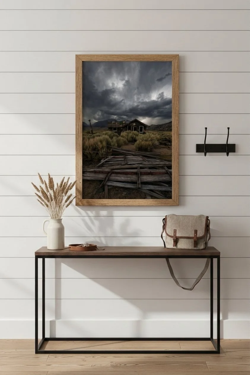 Fine art print of an abandoned Eastern Sierra cabin in a light wood frame hanging above a wooden console table on a white shiplap entryway wall.
