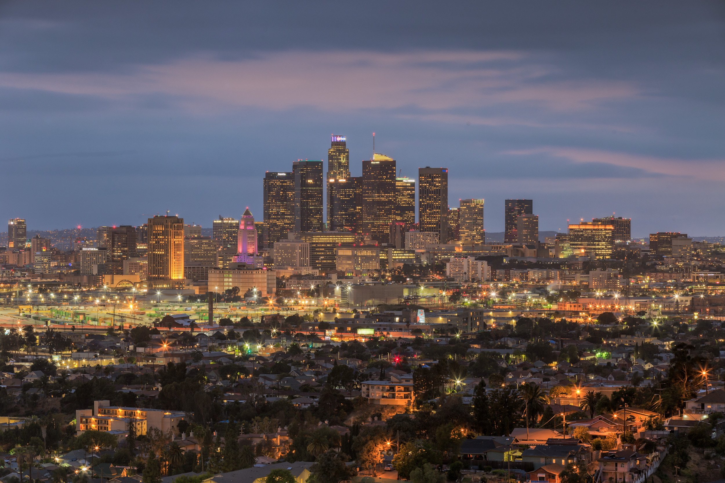 Panoramic night view of the Downtown Los Angeles skyline featuring the illuminated LA City Hall and city lights by Chris Ewen Crosby.