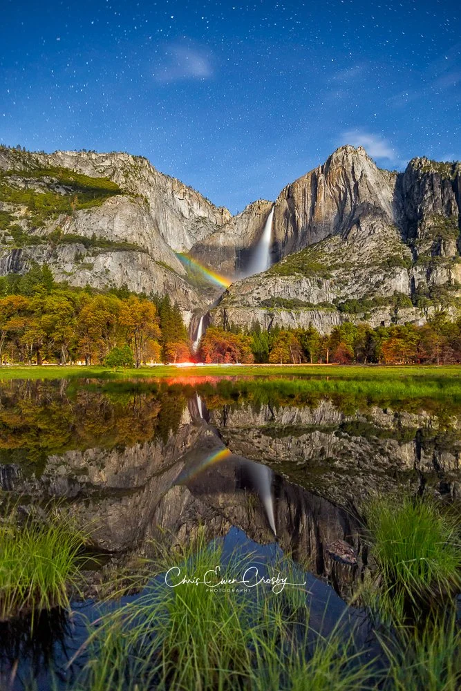 Long exposure night photography of a moonbow (lunar rainbow) over Yosemite Falls with a clear reflection in a pool of water in the foreground.