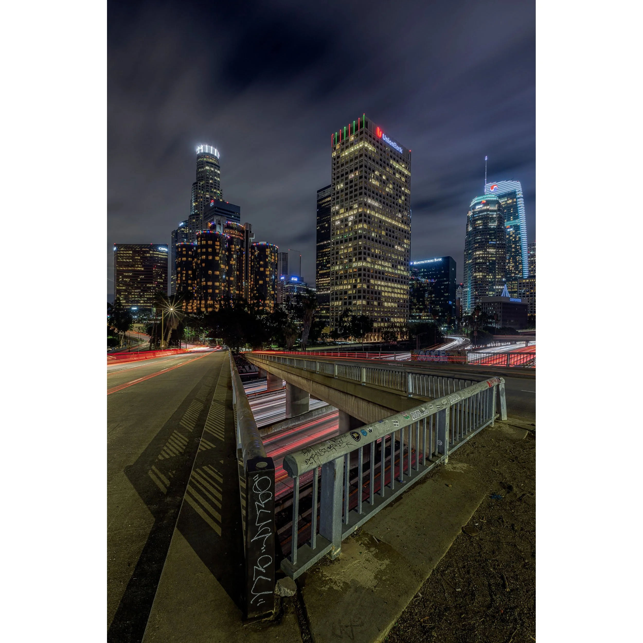 Vertical Downtown Los Angeles night photography featuring freeway light trails and city skyscrapers.