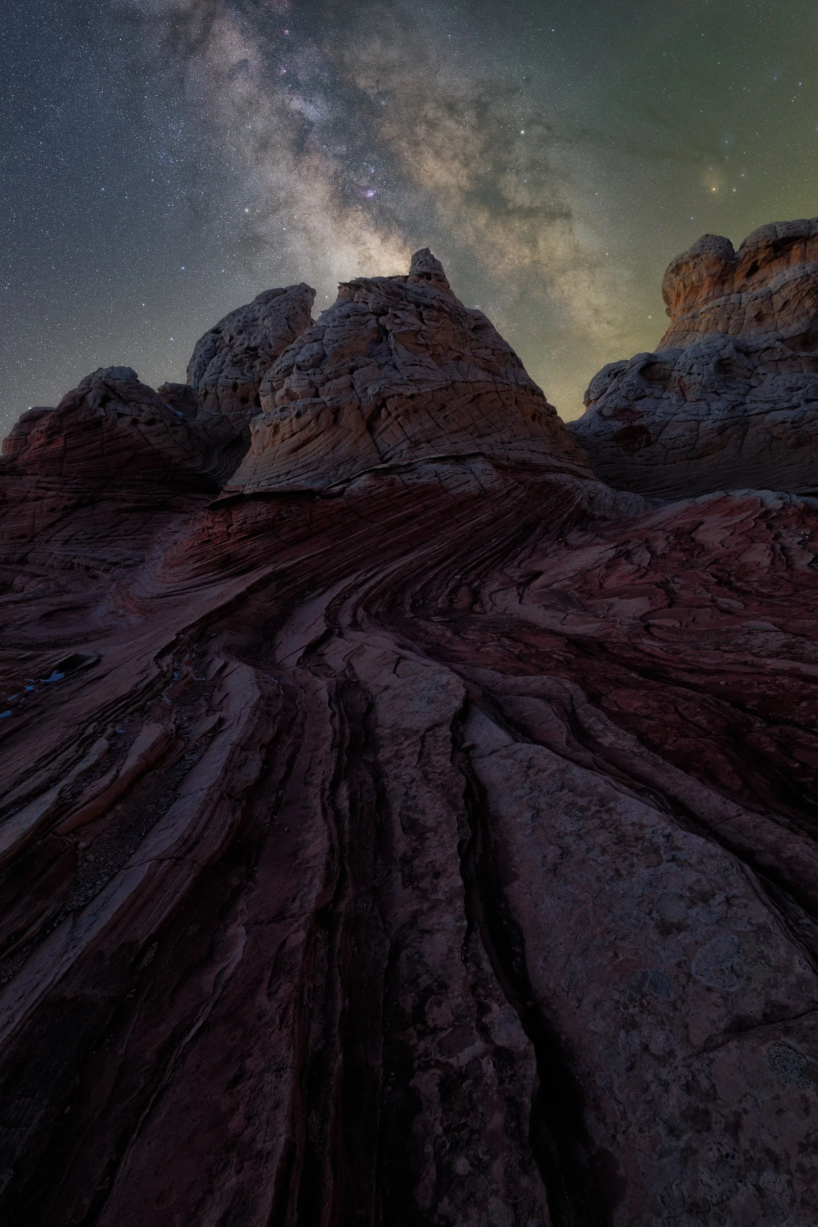 Vertical night astrophotography photograph of swirling red and white sandstone strata leading toward rock domes under the Milky Way at White Pocket in Vermilion Cliffs National Monument by Chris Ewen Crosby.