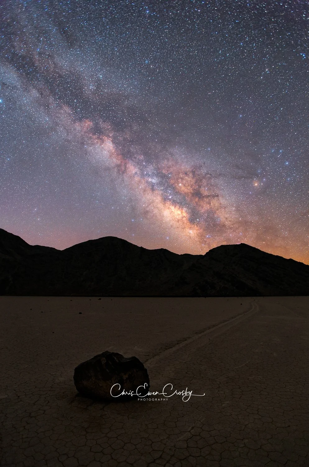 Vertical photo of a sliding rock and its trail on the cracked mud of Racetrack Playa in Death Valley National Park.