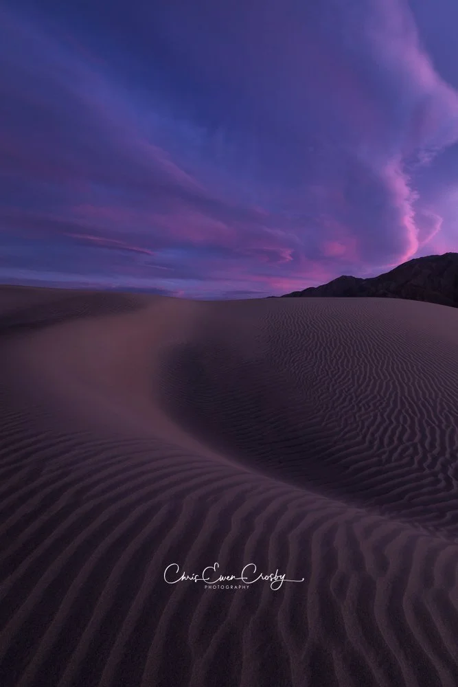 Vertical sunset photo of purple and orange sand dune ridges in Death Valley National Park.