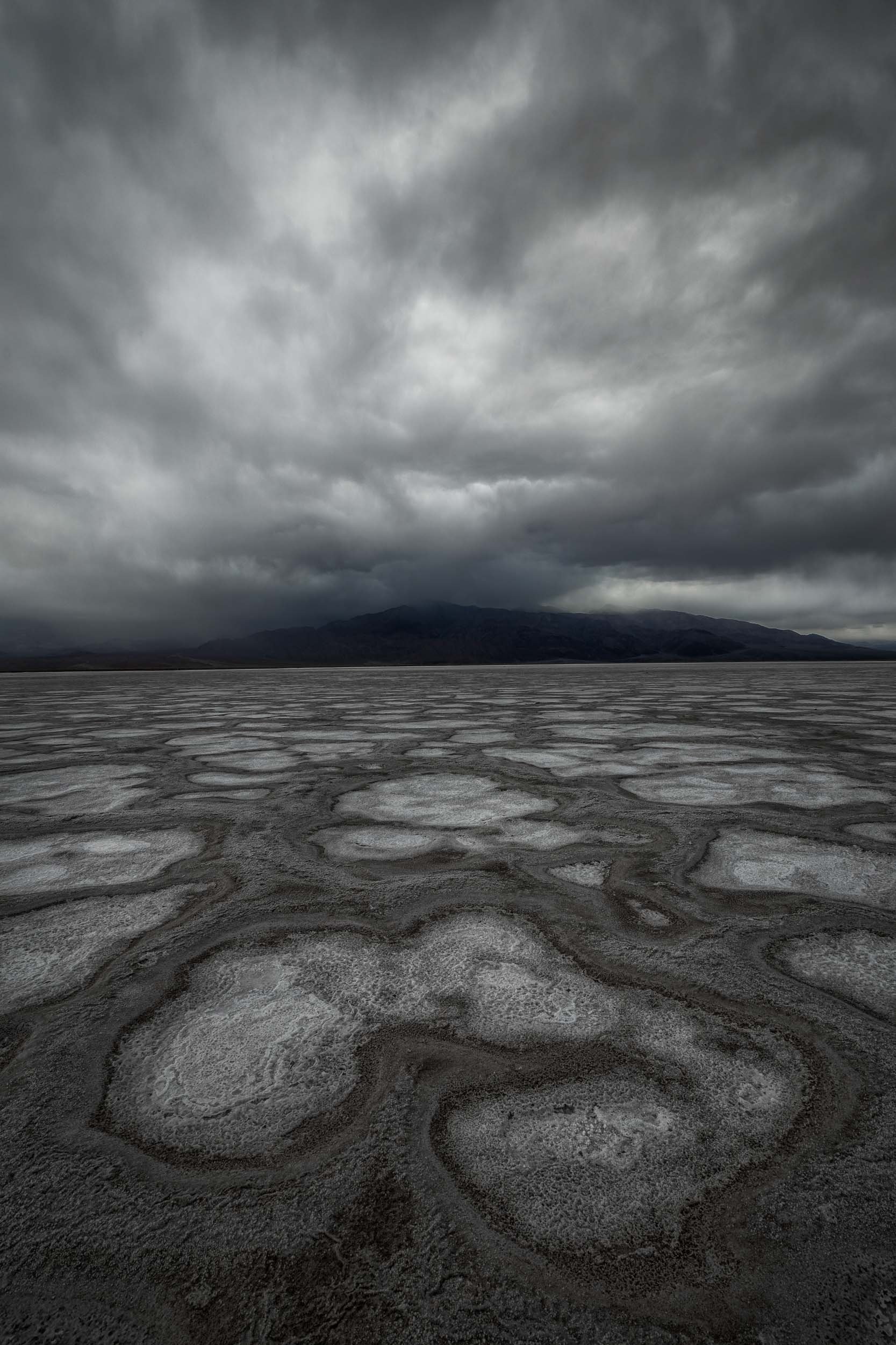 Textured salt formations under a dramatic, moody storm sky in Death Valley National Park.