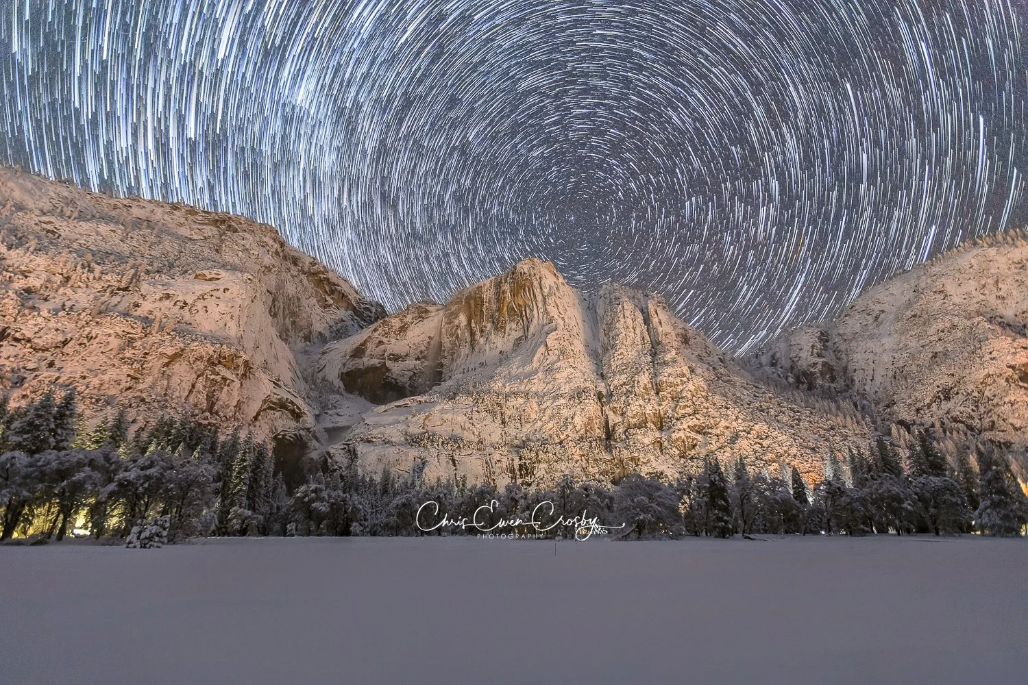3:2 landscape photo of star trails in a circular pattern over snow-covered Yosemite Falls at night in Yosemite National Park.