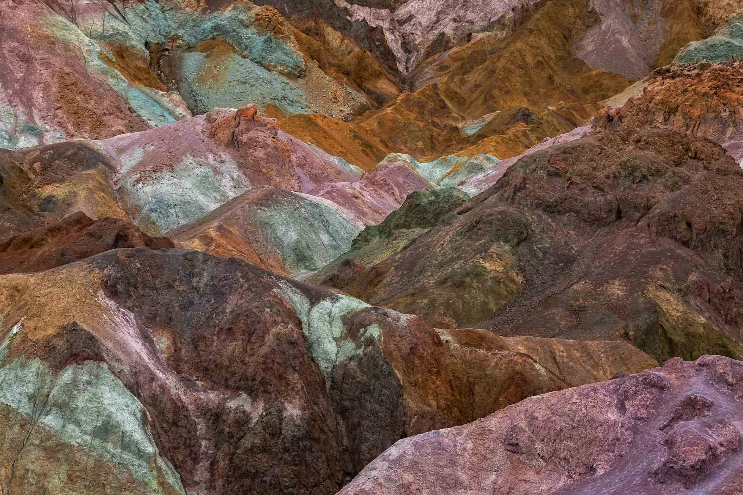 Abstract landscape view of the vibrant, colorful volcanic mineral hills of Artist's Palette in Death Valley National Park displaying hues of turquoise, pink, and gold.