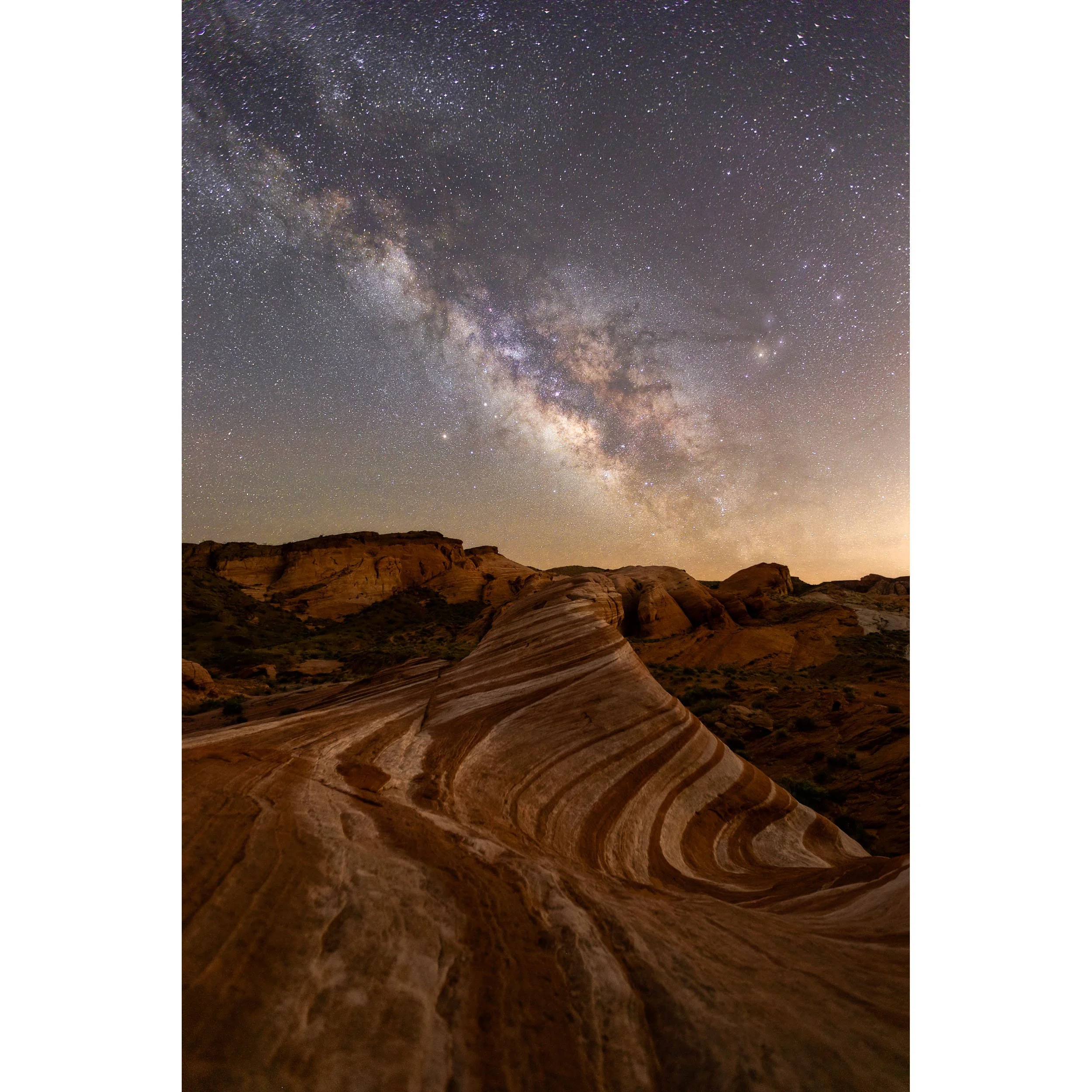 Vertical fine art night photograph of the bright Milky Way galaxy arching over the striped sandstone formations of the Fire Wave in Valley of Fire State Park.