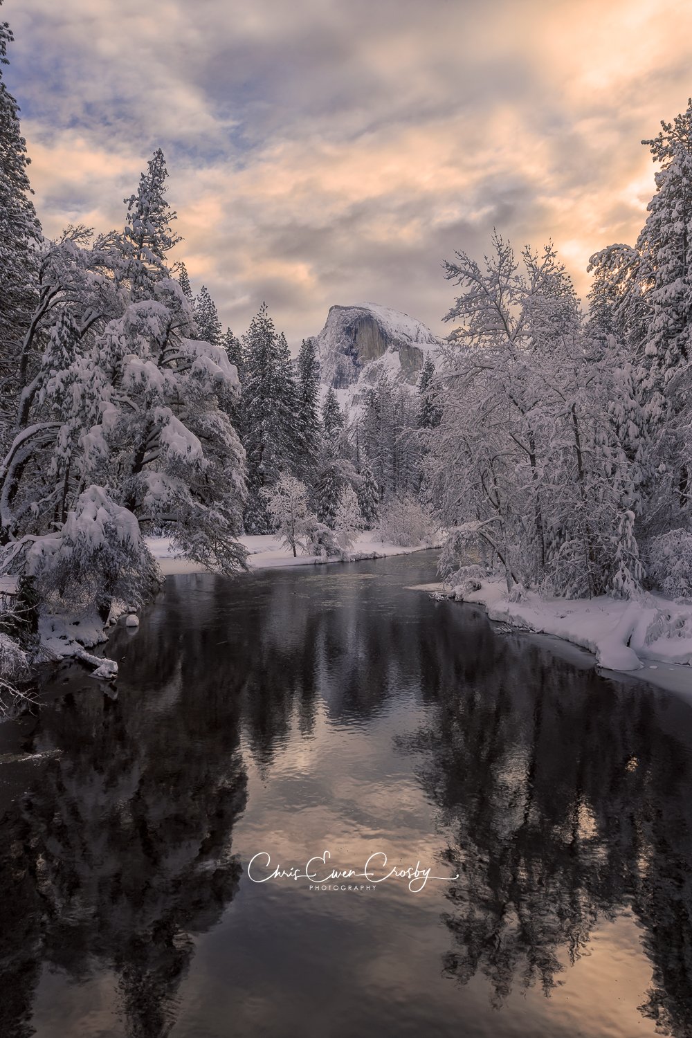 A vertical landscape of Yosemite National Park featuring the Merced River leading toward Half Dome under a soft, glowing morning sky.