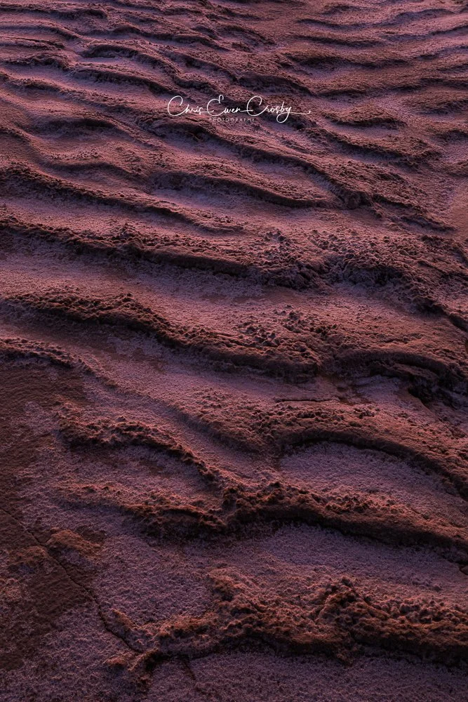 Vertical abstract photo of cracked desert mud glowing with fiery sunset light and white salt dusting.