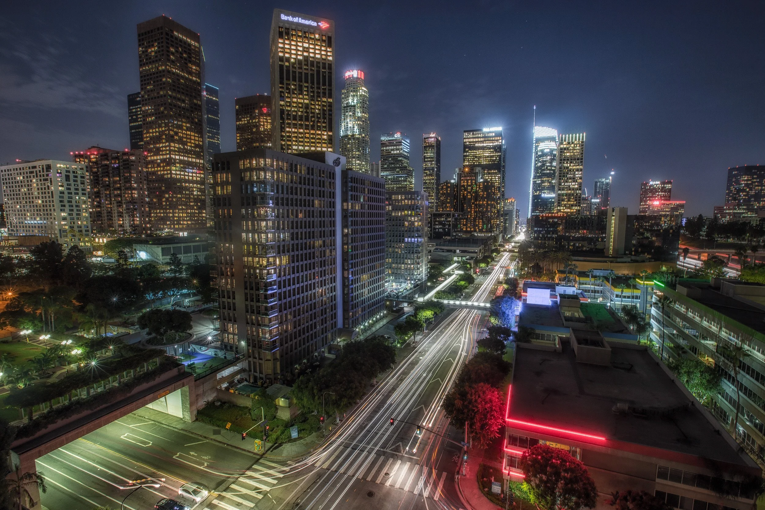 High-angle long exposure of traffic light trails on Flower Street leading into the illuminated Downtown Los Angeles skyline at night by Chris Ewen Crosby.