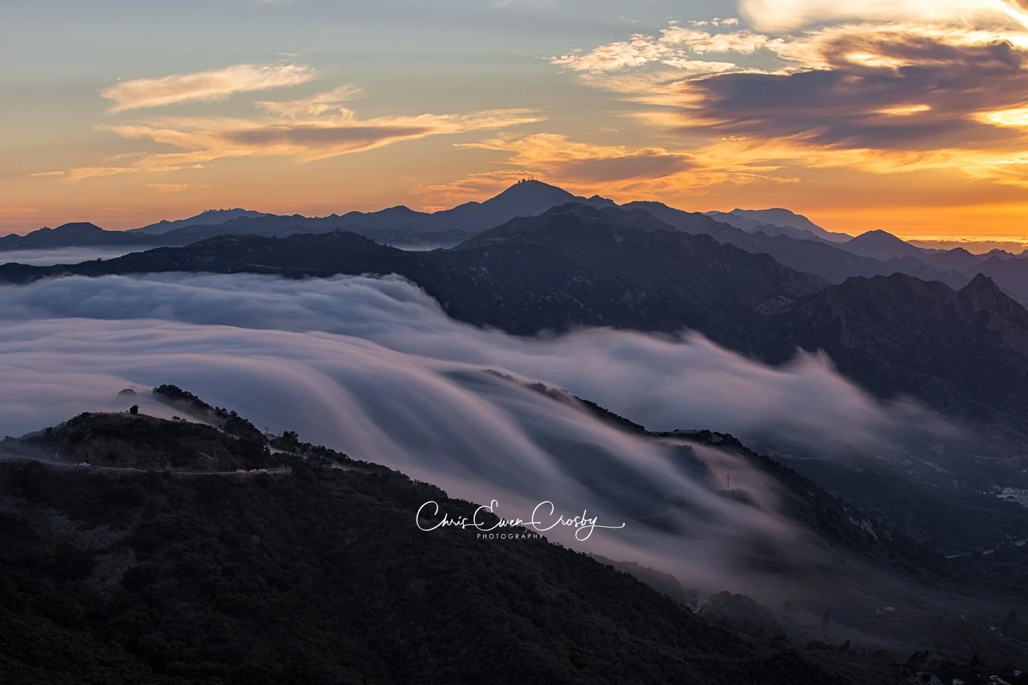 Long exposure of a fog wave spilling over Southern California Mountains at sunset; 3:2 landscape with silky white mist.