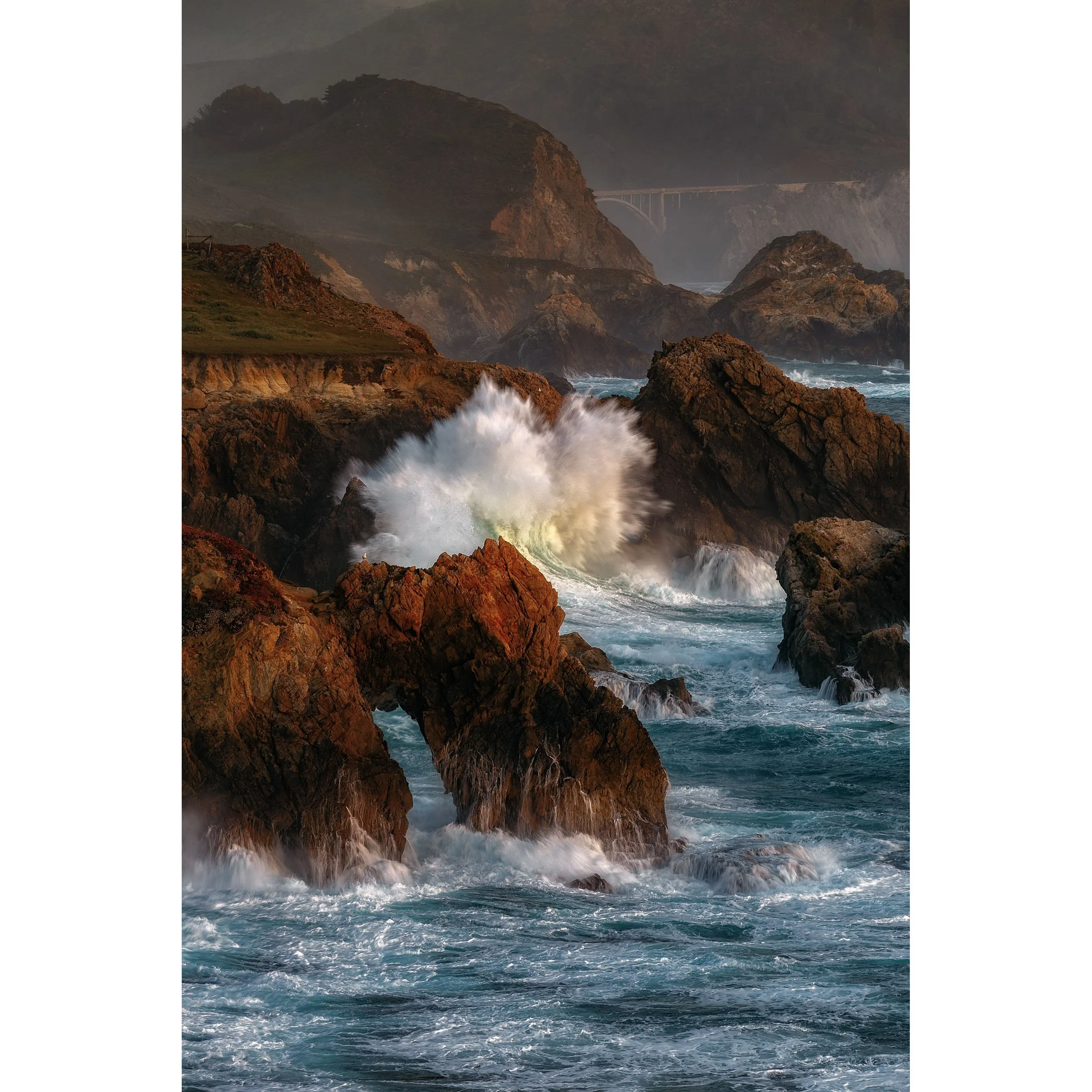 Vertical coastal photo of an explosive wave crashing against rugged Big Sur sea stacks at sunset.