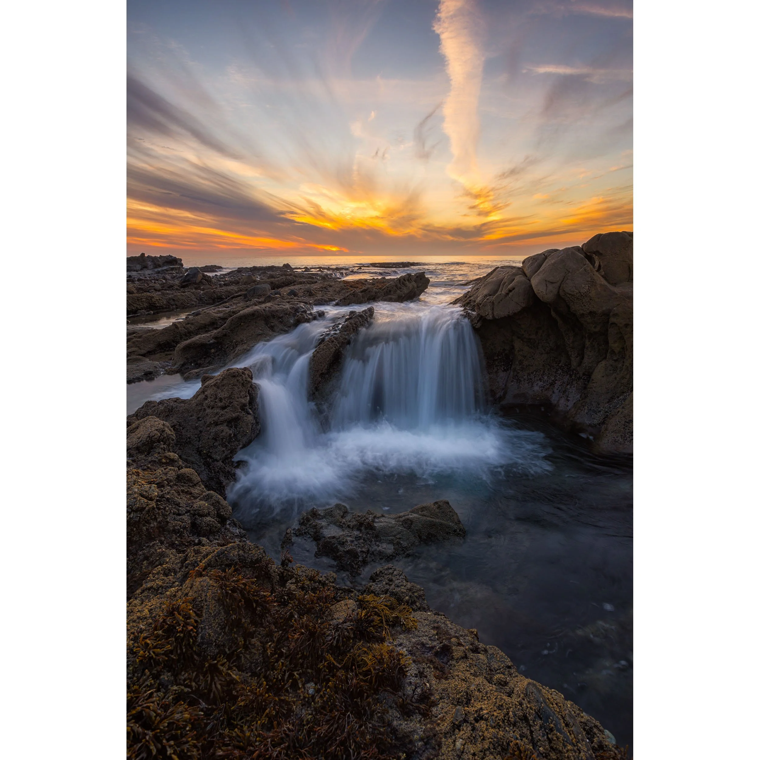 Vertical ocean landscape photo of cascading tide pool waterfalls at sunset in Laguna Beach.