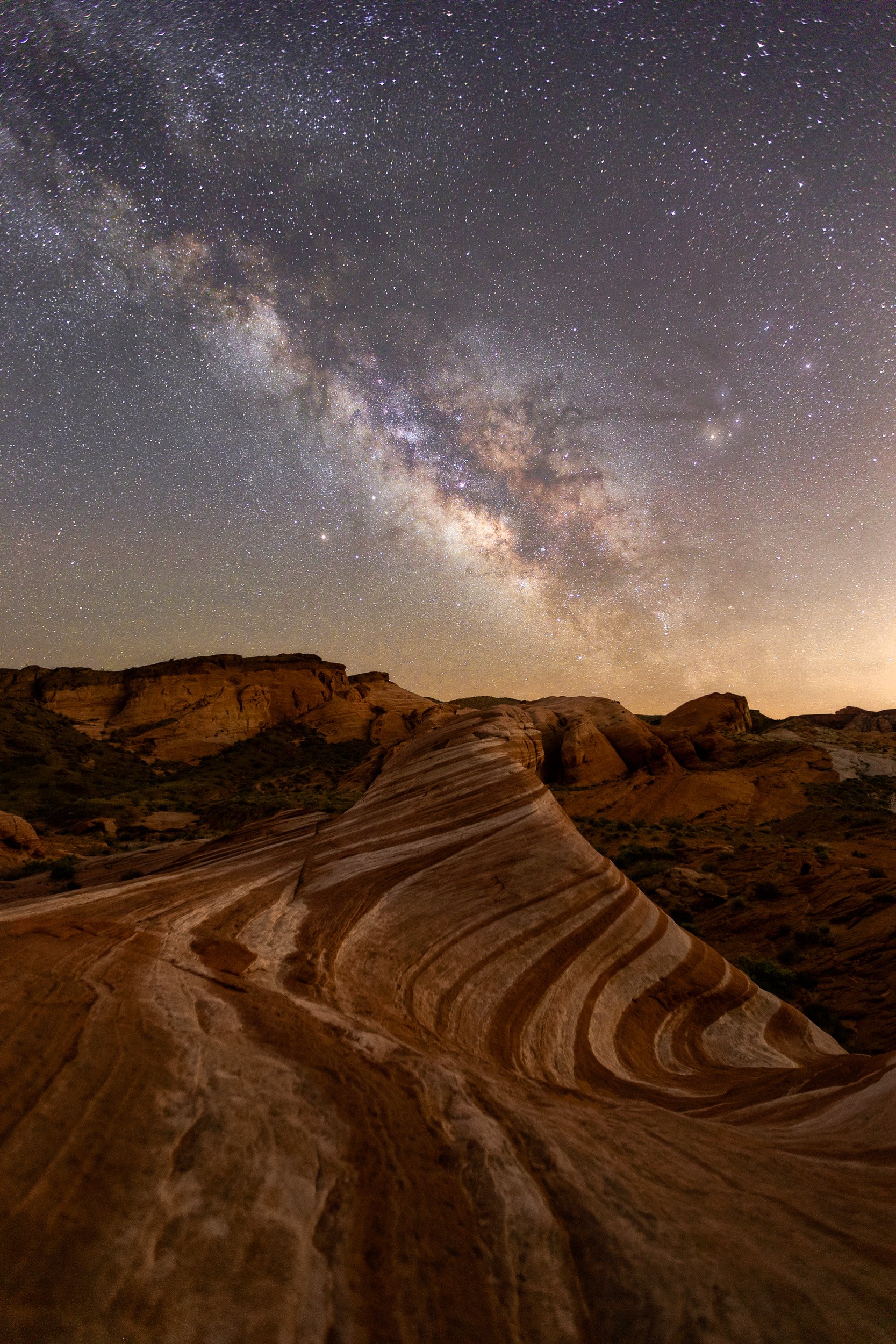 Vertical night astrophotography photograph of the striped sandstone swirls at Fire Wave pointing toward the Milky Way galaxy in Valley of Fire State Park, Nevada by Chris Ewen Crosby.