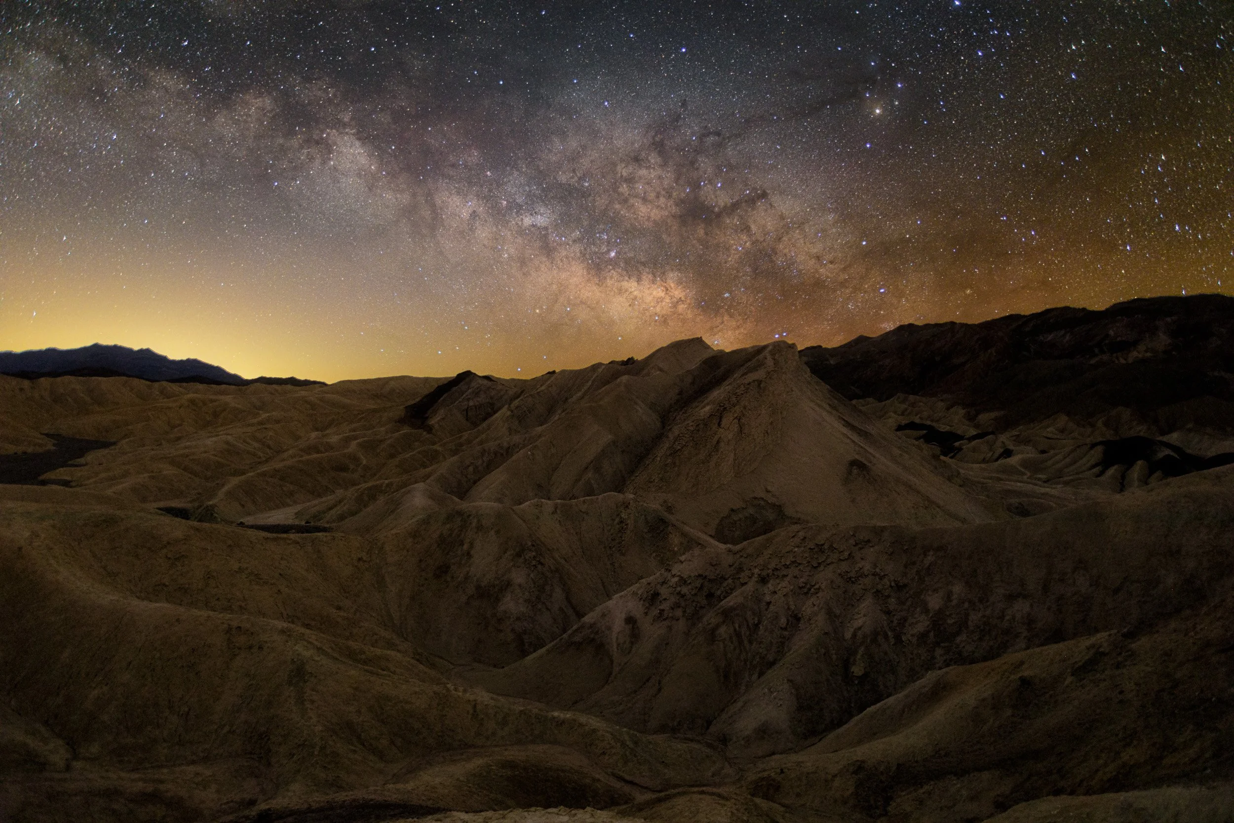 Wide-angle night landscape photograph showcasing the vibrant Milky Way core arching over the desert badlands of Death Valley under a dark, starry sky during the March photography masterclass.