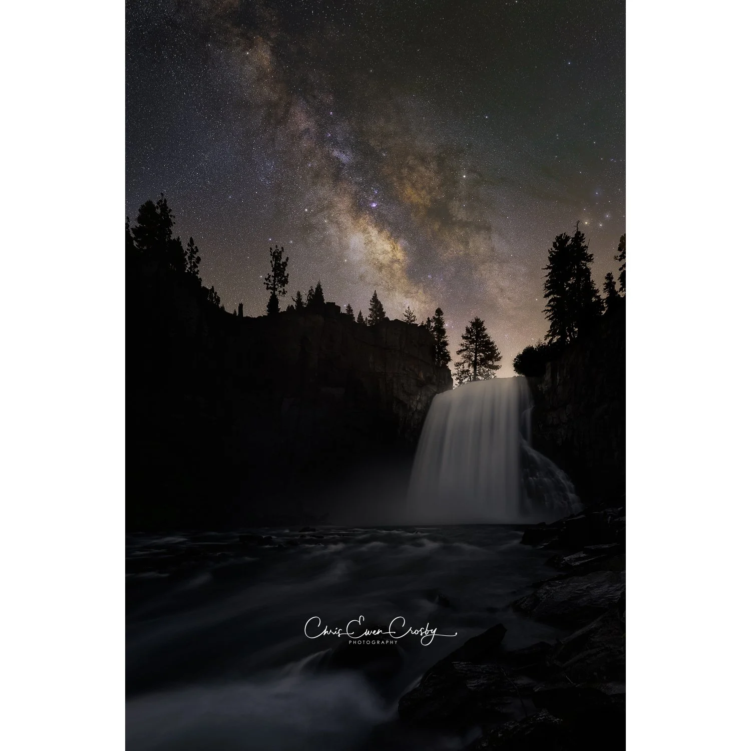 A high-resolution vertical night photograph of Rainbow Falls in Mammoth Lakes with the Milky Way galaxy core glowing intensely above the rushing waterfall and mist.