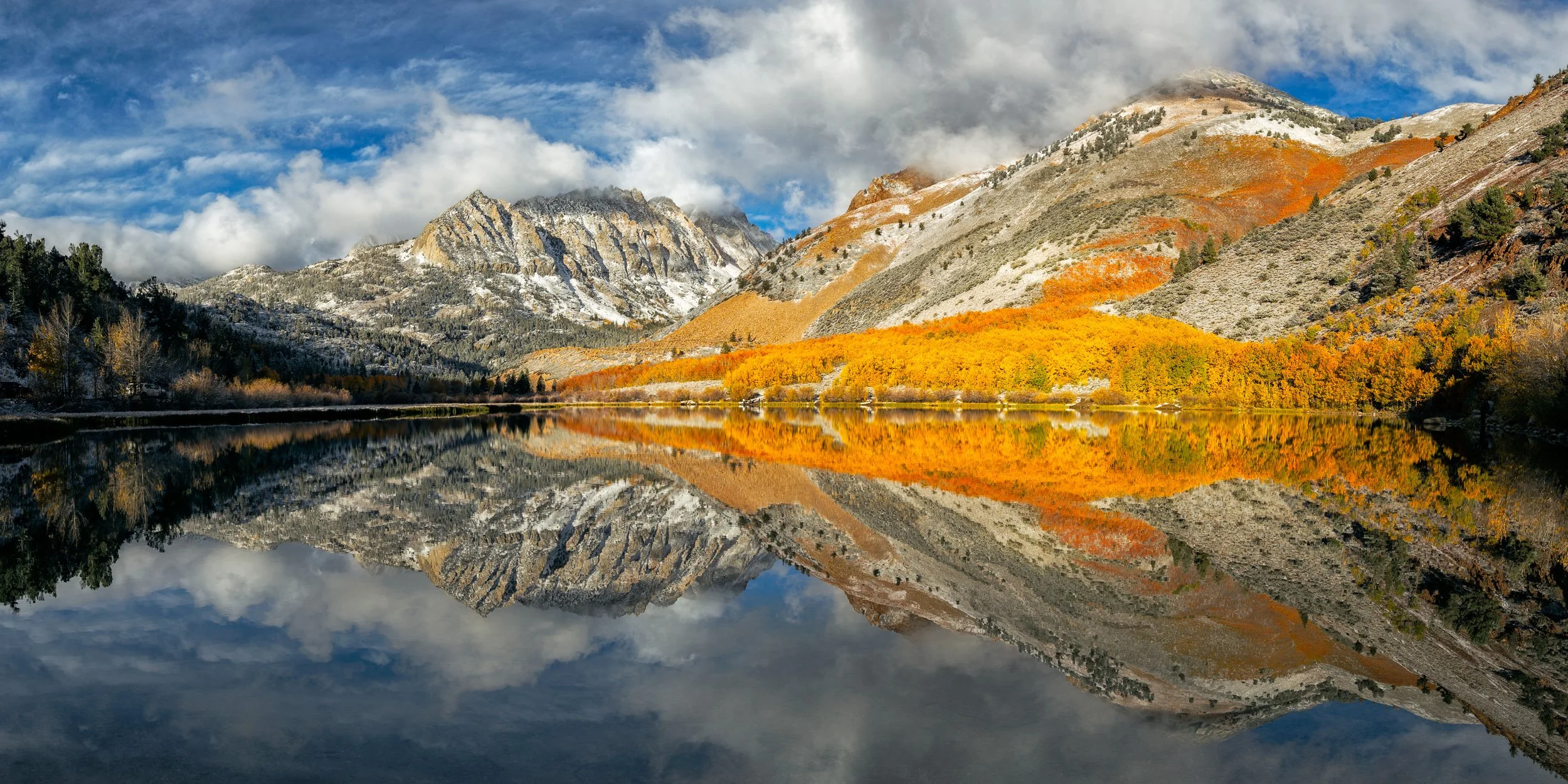 Panoramic landscape photograph of vibrant golden autumn aspens and snow-dusted Sierra Nevada mountains reflected perfectly in glass-like North Lake by Chris Ewen Crosby.