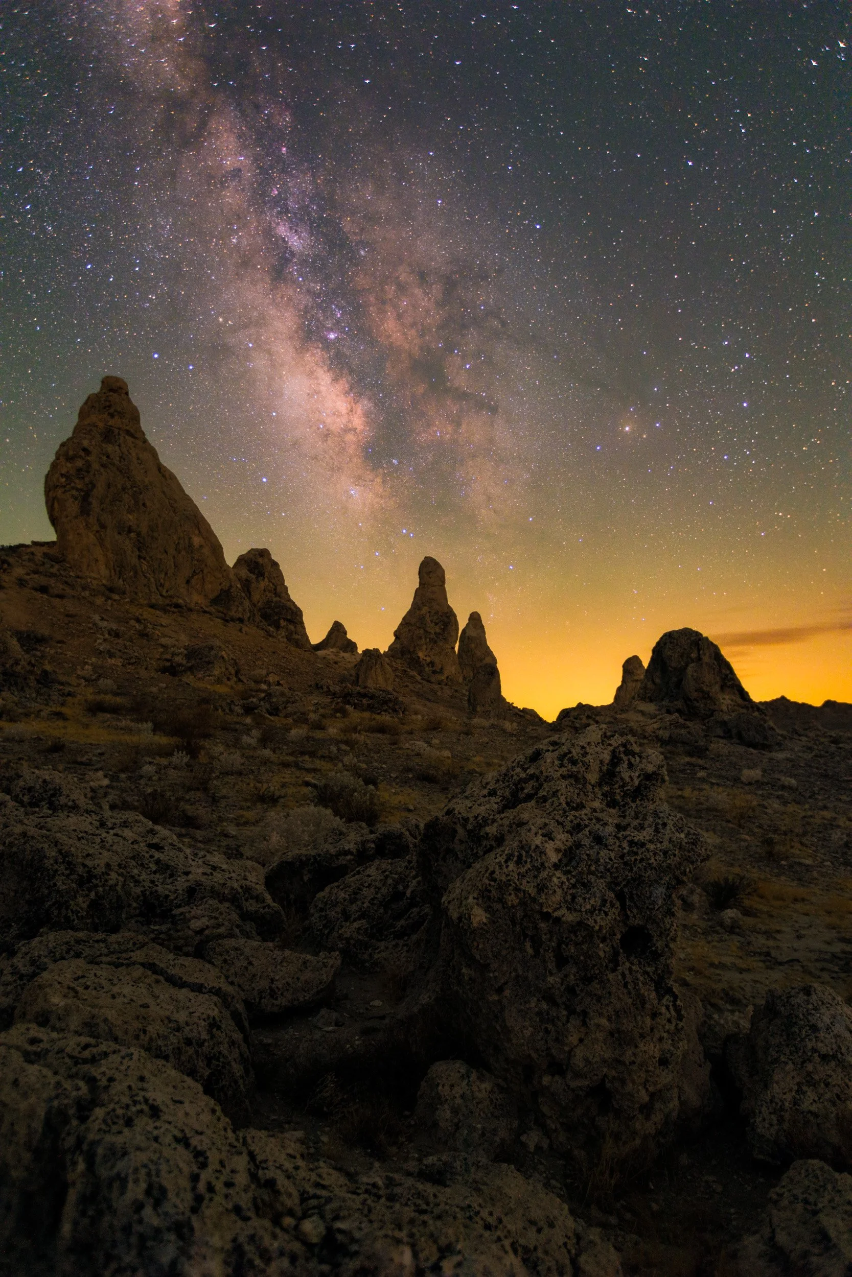 Vertical night astrophotography photograph of rugged tufa spires silhouetted beneath the glowing Milky Way galaxy core at the Trona Pinnacles near Ridgecrest, California by Chris Ewen Crosby.