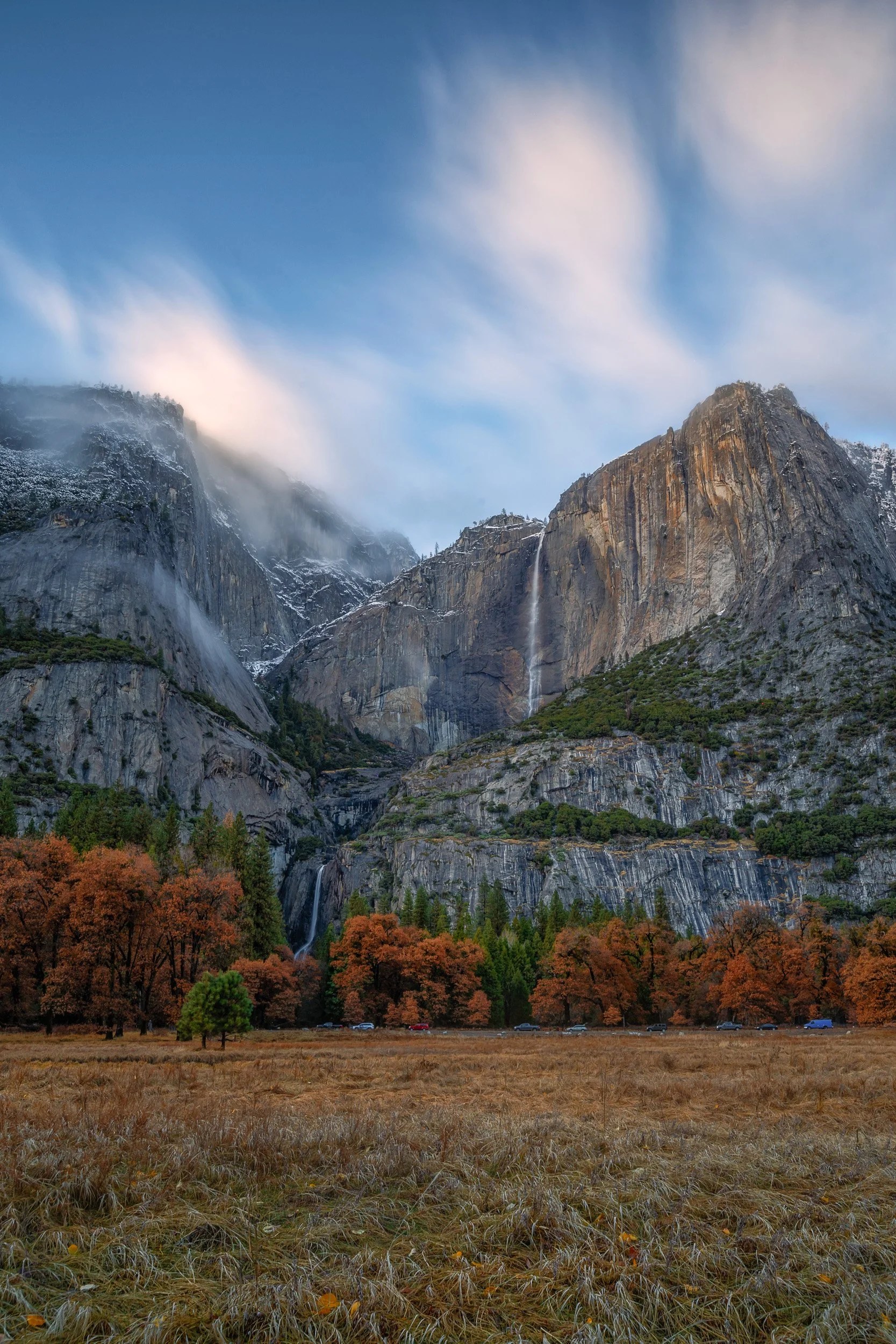 Autumn orange trees in a dry meadow below Yosemite Falls with dynamic clearing clouds during an autumn photography workshop.