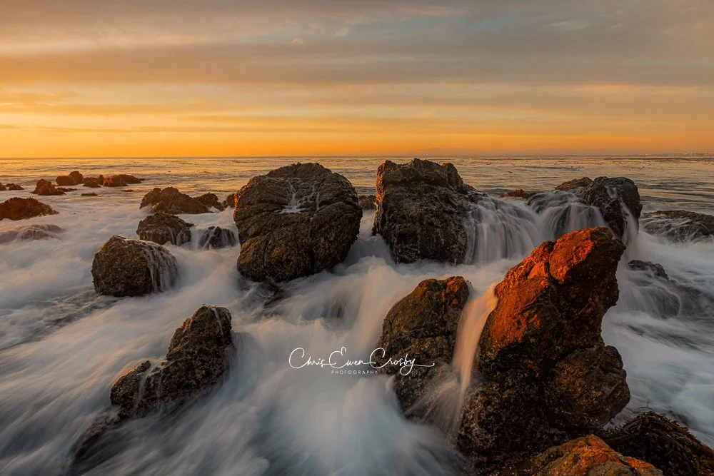 Landscape sunset photo of silky golden waves flowing around dark sea stacks on a California beach.