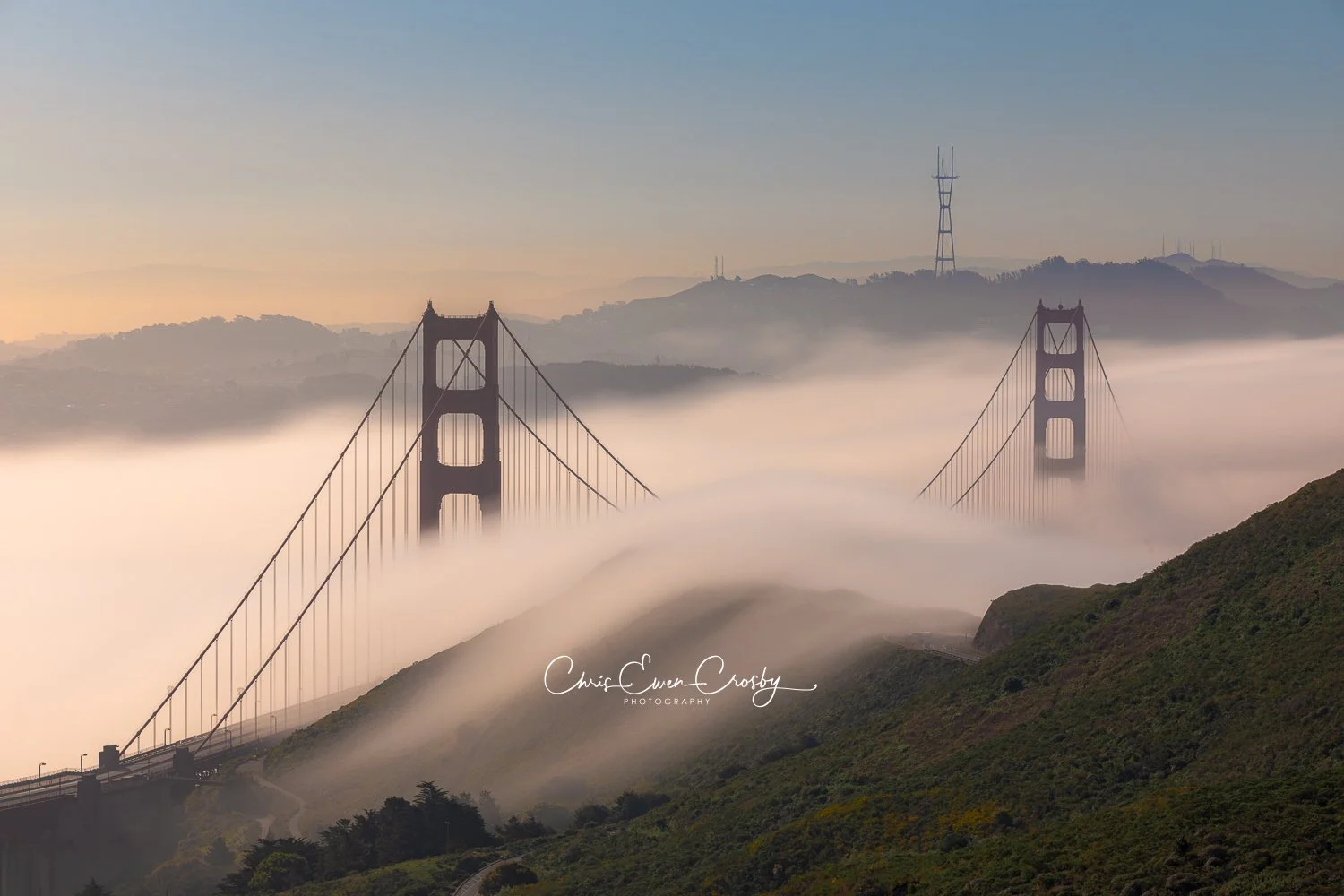 A horizontal long exposure photograph titled "Golden Flows" showing the red towers of the Golden Gate Bridge rising above a thick, silky white fog flowing through the San Francisco Bay.