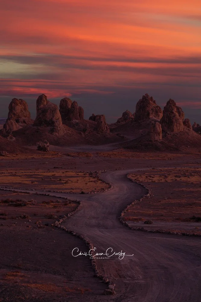 Vertical 2:3 photo of jagged desert tufa pinnacles at sunset with a dramatic sky of orange, red, and purple clouds.