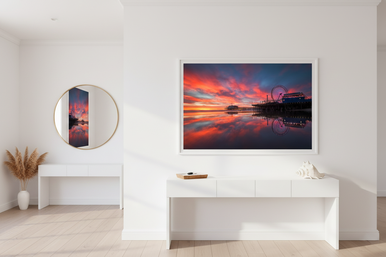 Framed vibrant California pier print hanging above a travertine bench in a sunlit entryway.