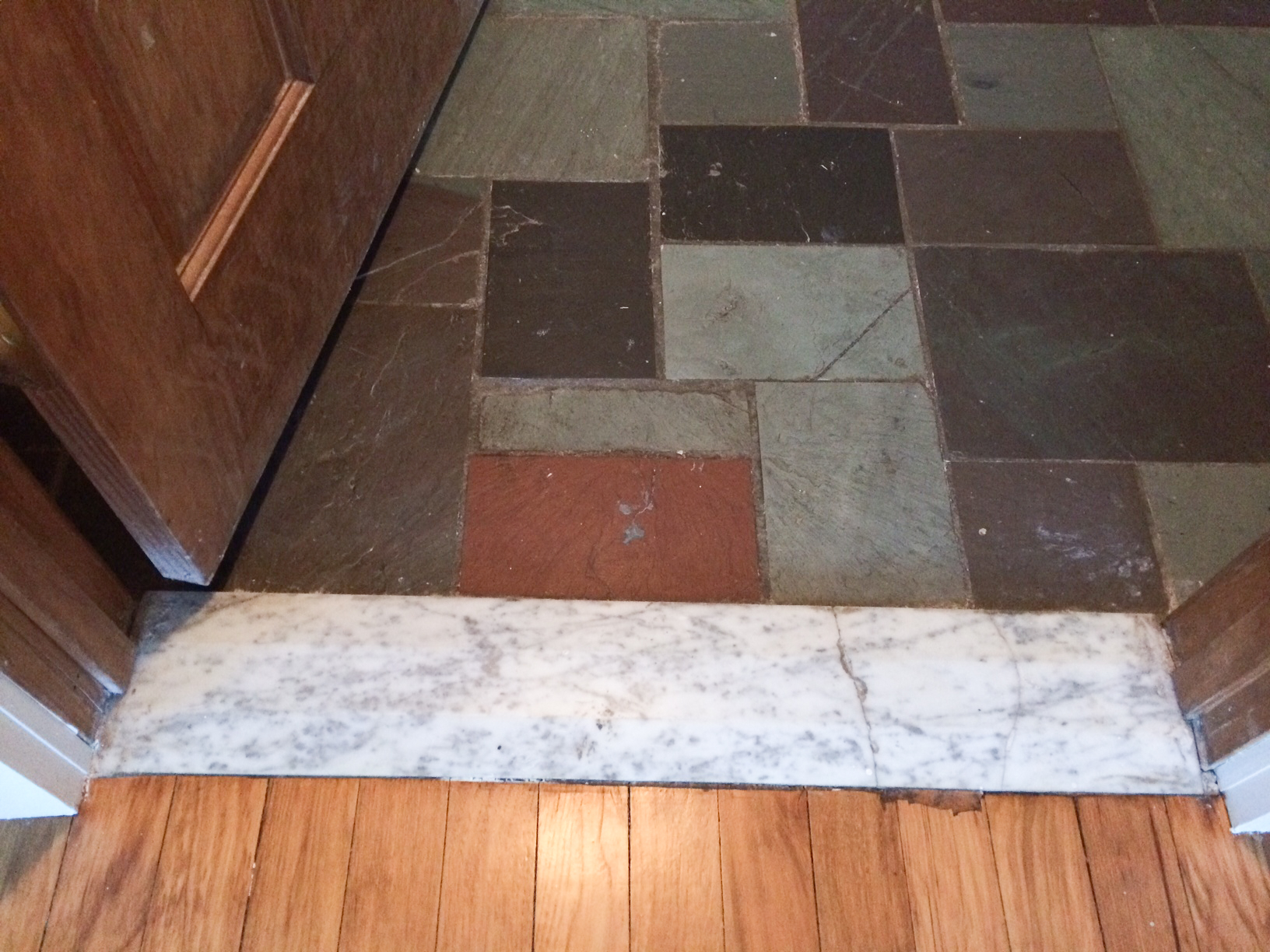 Wood floor from the adjoining room transitions to flagstone via this cracked marble threshold.