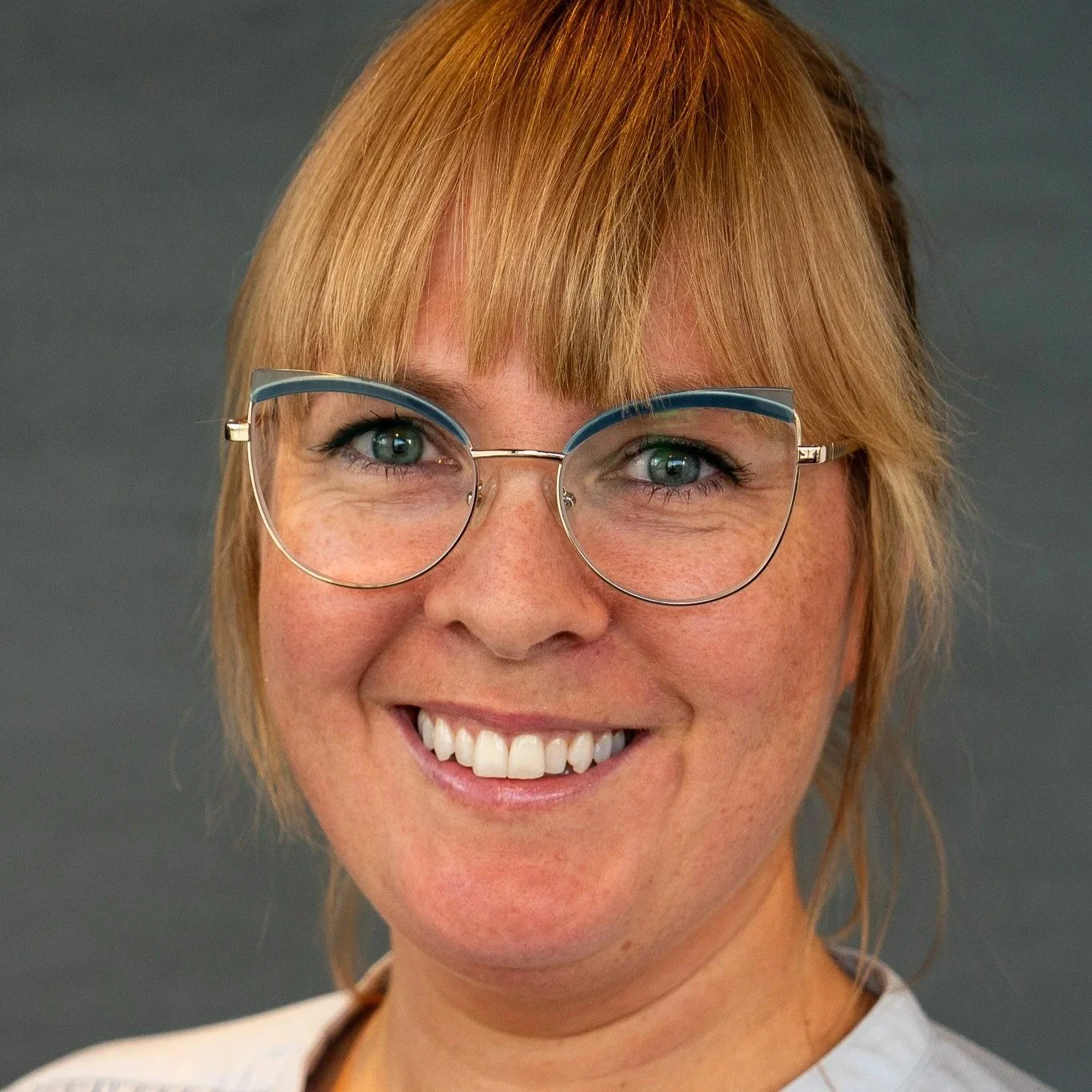 Nærbilde av en smilende kvinne med blondt hår og brillor.