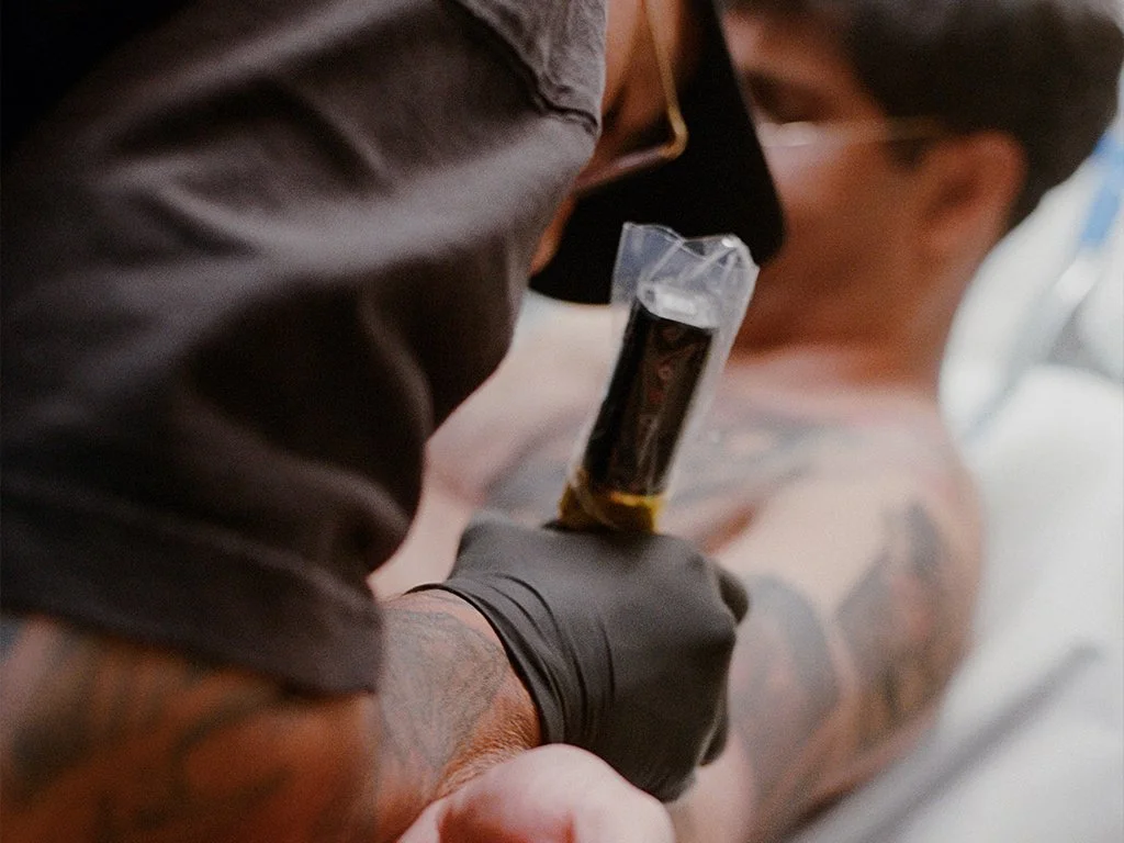 Tattoo artist Esteban Caasi working on a client’s arm inside his private Brooklyn studio, showing close up detail of the tattooing process.