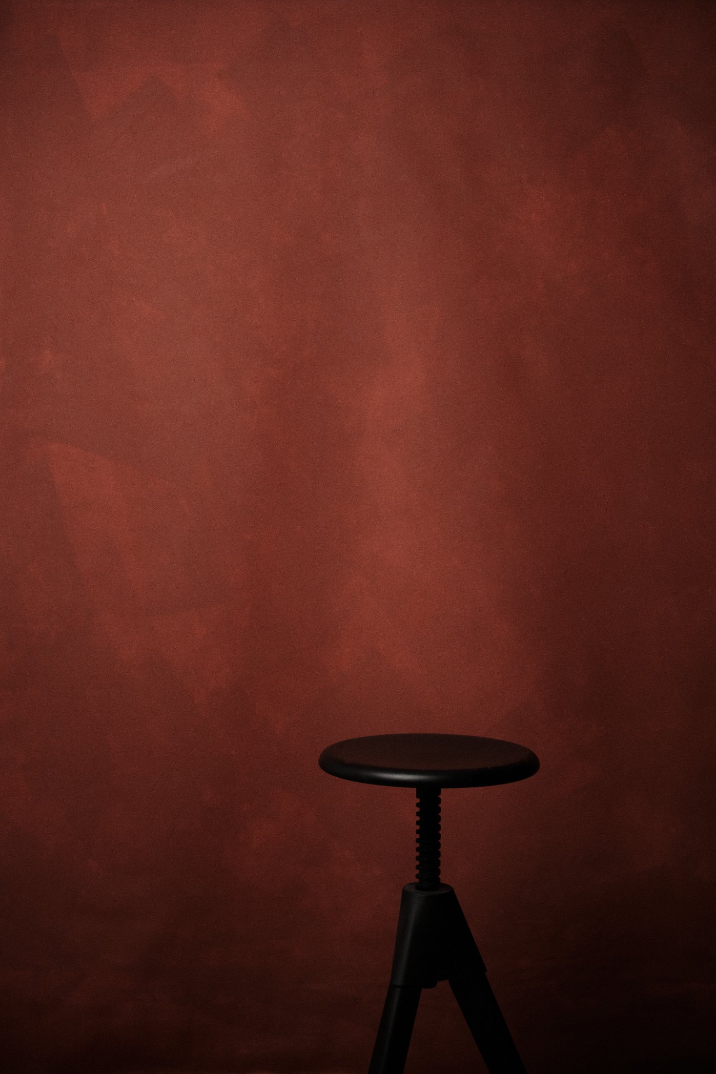 Reduzierter Studiohintergrund in warmem Rotton mit schwarzem Hocker, fotografiert im Fotostudio bei ruhigem Licht.