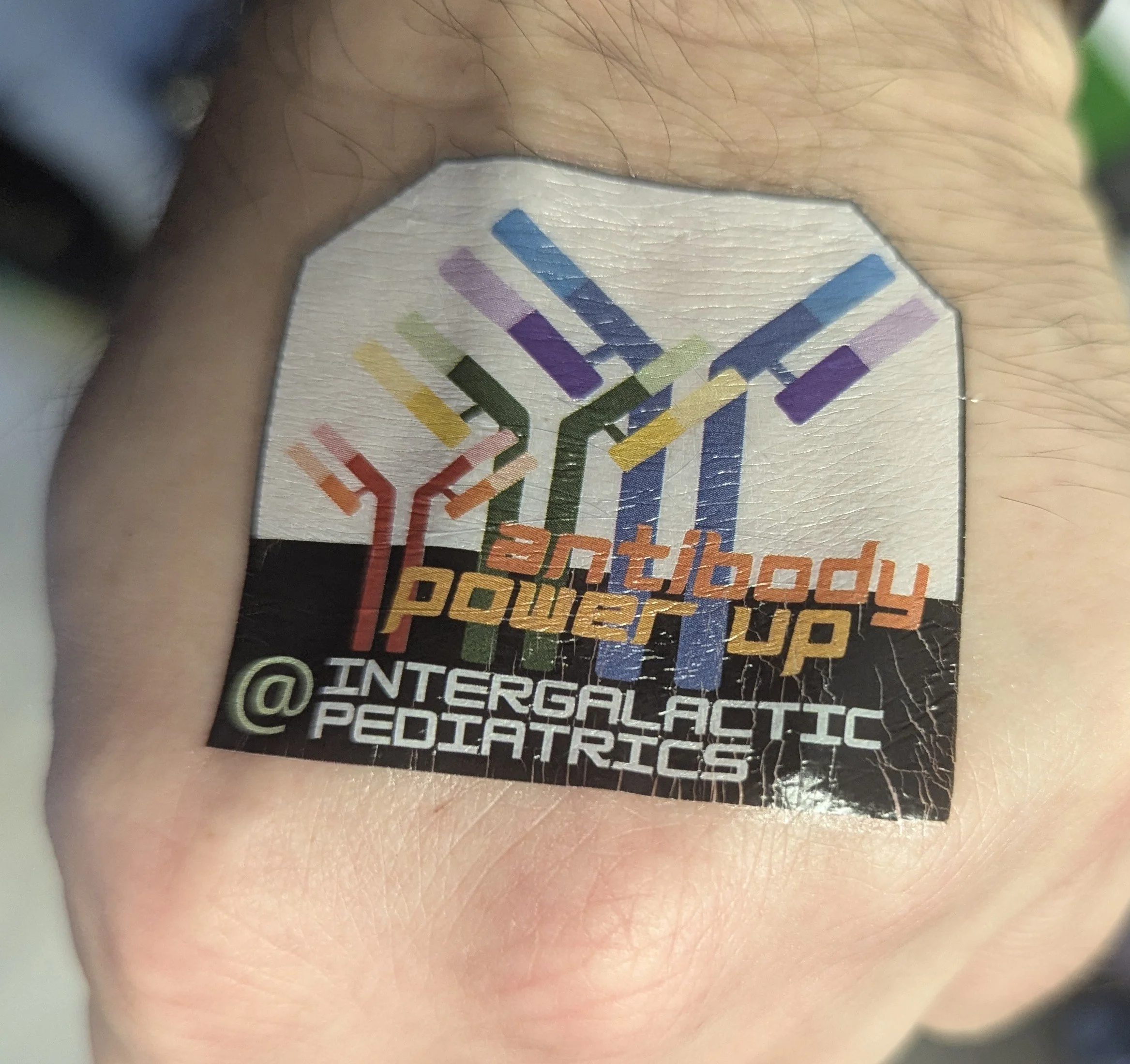 Temporary tattoo with "antibody power up @ intergalactic pediatrics" and 3 antibodies of increasing size in a rainbow spectrum