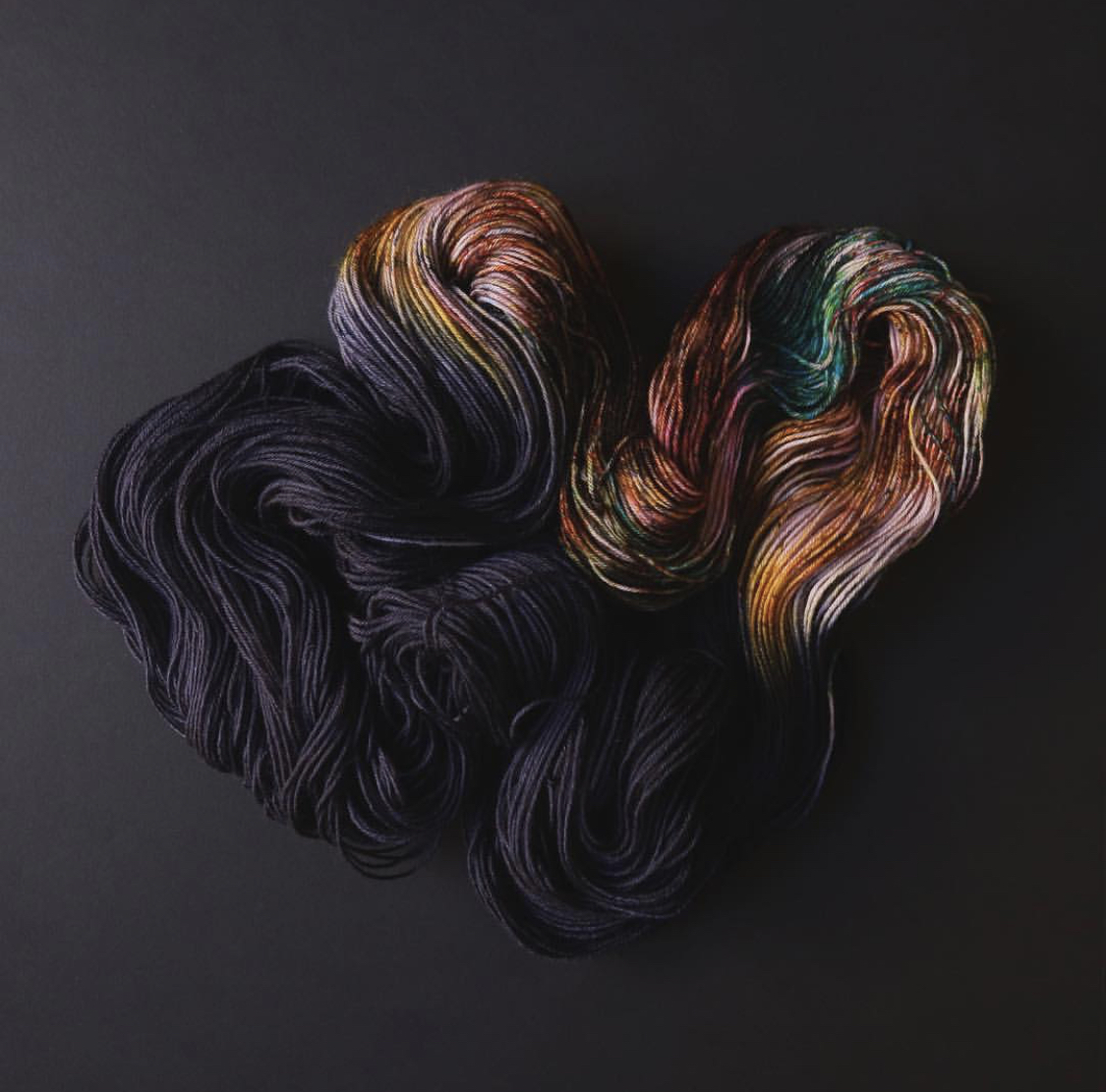 An unskeined hank of dark navy yarn with a section of speckled pink flows across a black background; Photo by Tayler Earl of Fiber for the People®