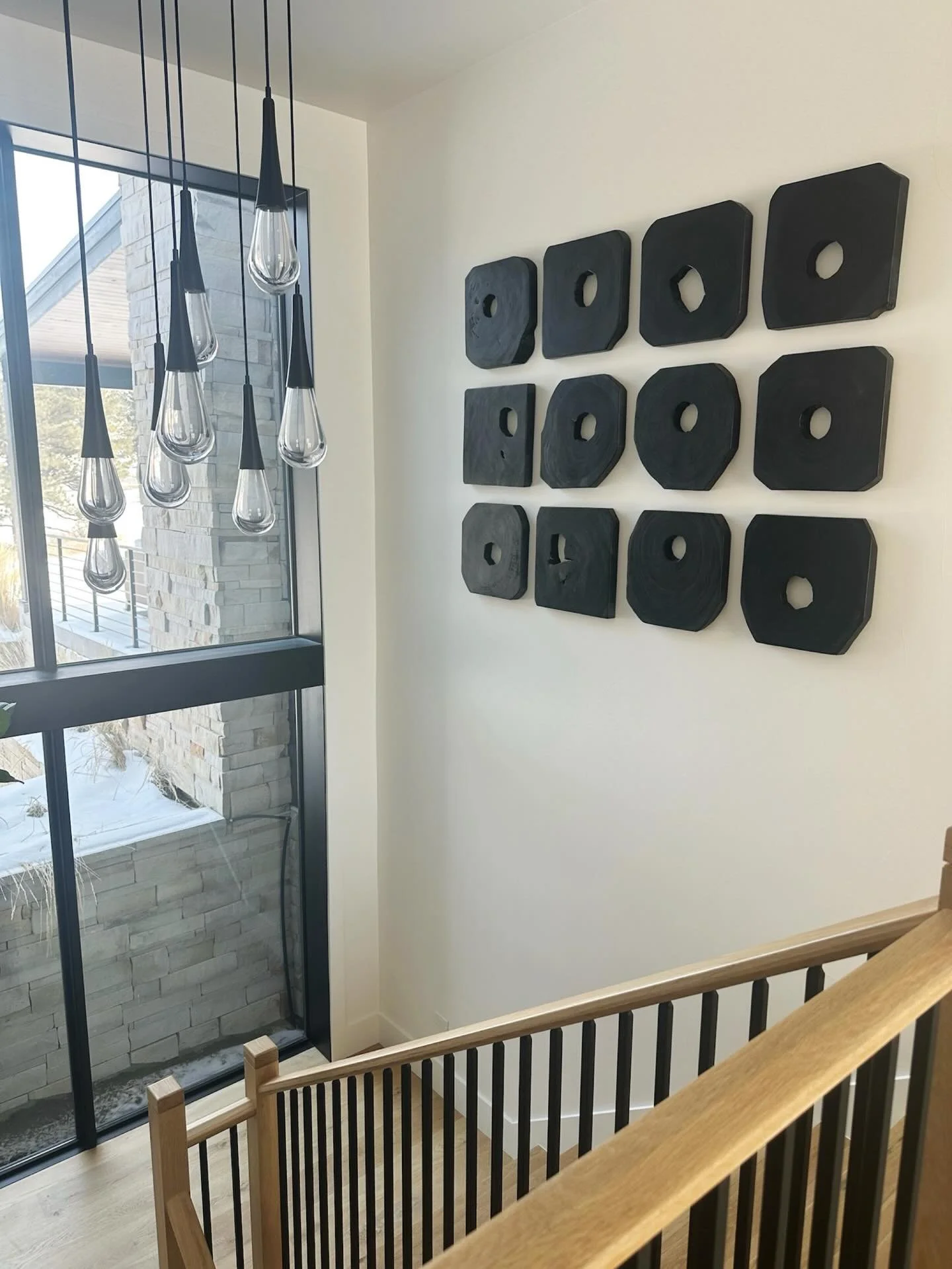 Loving how this stairwell art piece turned out! We chose dimensional wood slices to add visual interest without distracting from the beautiful view and natural light. This piece perfectly complements the home&rsquo;s warm, inviting vibe while keeping