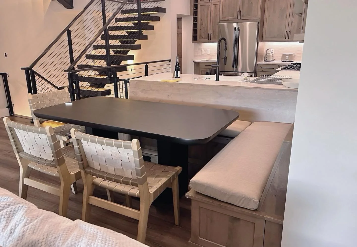 Gathered around the table, connected by design. This custom built-in banquette flows seamlessly from the kitchen island, creating a cozy and functional dining nook in the heart of our mountain modern kitchen. Warm wood tones, woven leather chairs, an
